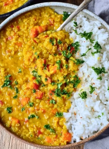 Bowl of creamy red lentil dahl with spices and herbs on a wooden table.