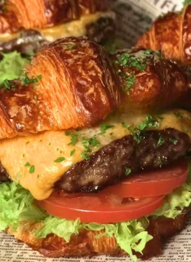 Delicious croissant smash burger with toppings on a wooden table