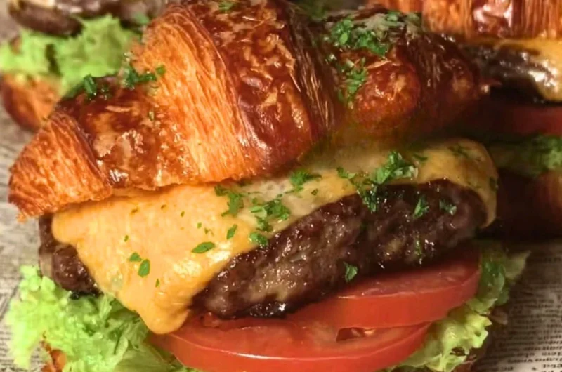 Delicious croissant smash burger with toppings on a wooden table