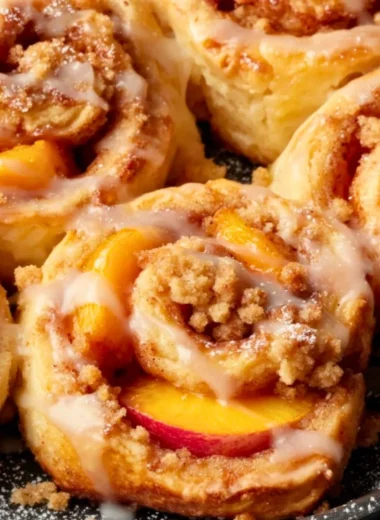 Delicious peach cobbler cinnamon rolls topped with glaze and fresh peaches