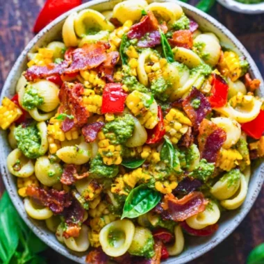 Summer pasta salad with corn, bell pepper, bacon, and creamy pesto dressing in a bowl.