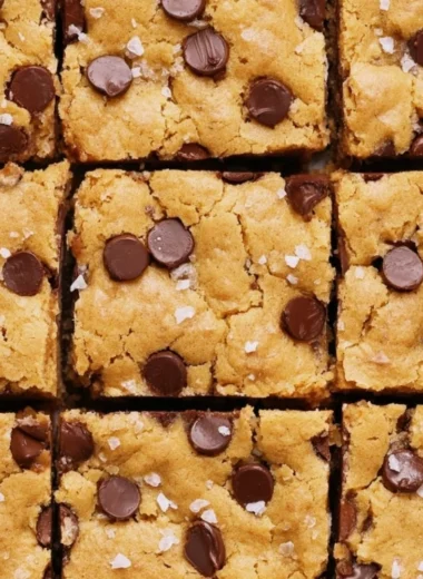 Ultimate blondies topped with chocolate chips and nuts on a wooden table.