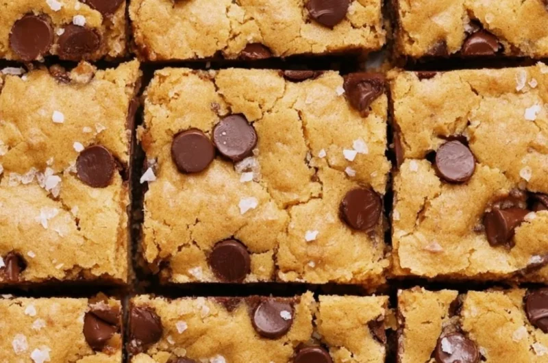 Ultimate blondies topped with chocolate chips and nuts on a wooden table.