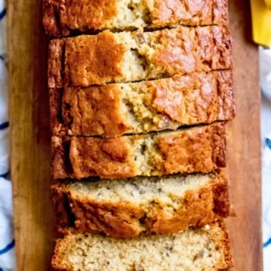 Delicious loaf of banana bread served with sliced bananas and nuts.