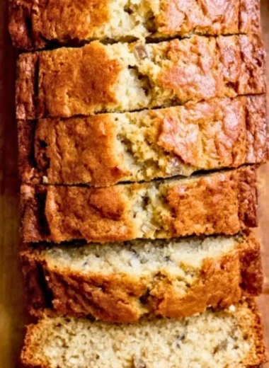 Delicious loaf of banana bread served with sliced bananas and nuts.