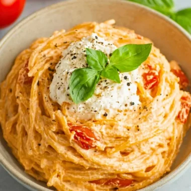 Roasted tomato and garlic ricotta pasta in a bowl, garnished with fresh herbs.