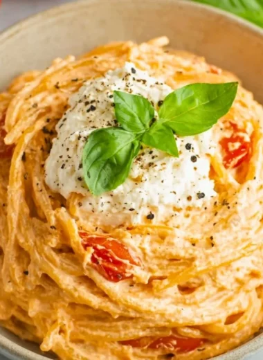 Roasted tomato and garlic ricotta pasta in a bowl, garnished with fresh herbs.