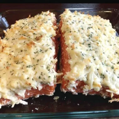 Baked salmon with mayo, Parmesan, and herbs on a plate, garnished with lemon.