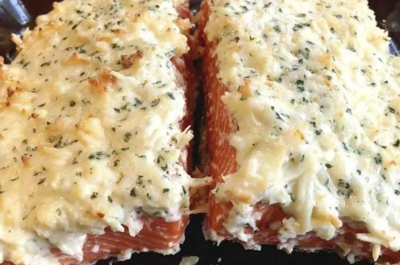 Baked salmon with mayo, Parmesan, and herbs on a plate, garnished with lemon.