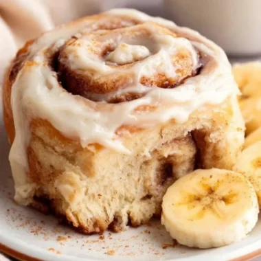 Delicious banana bread cinnamon rolls topped with creamy icing on a plate.