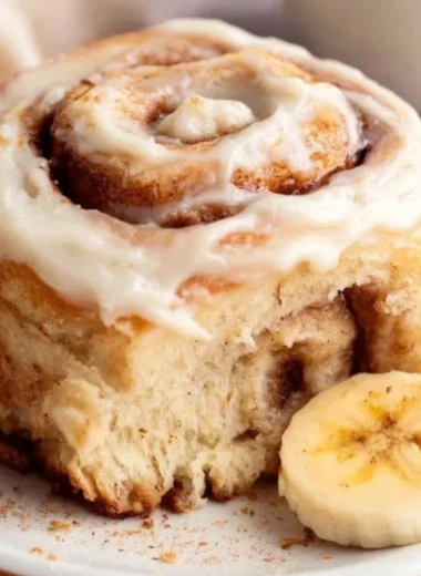 Delicious banana bread cinnamon rolls topped with creamy icing on a plate.