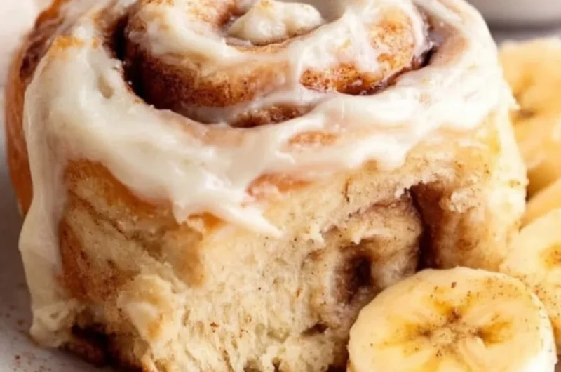 Delicious banana bread cinnamon rolls topped with creamy icing on a plate.